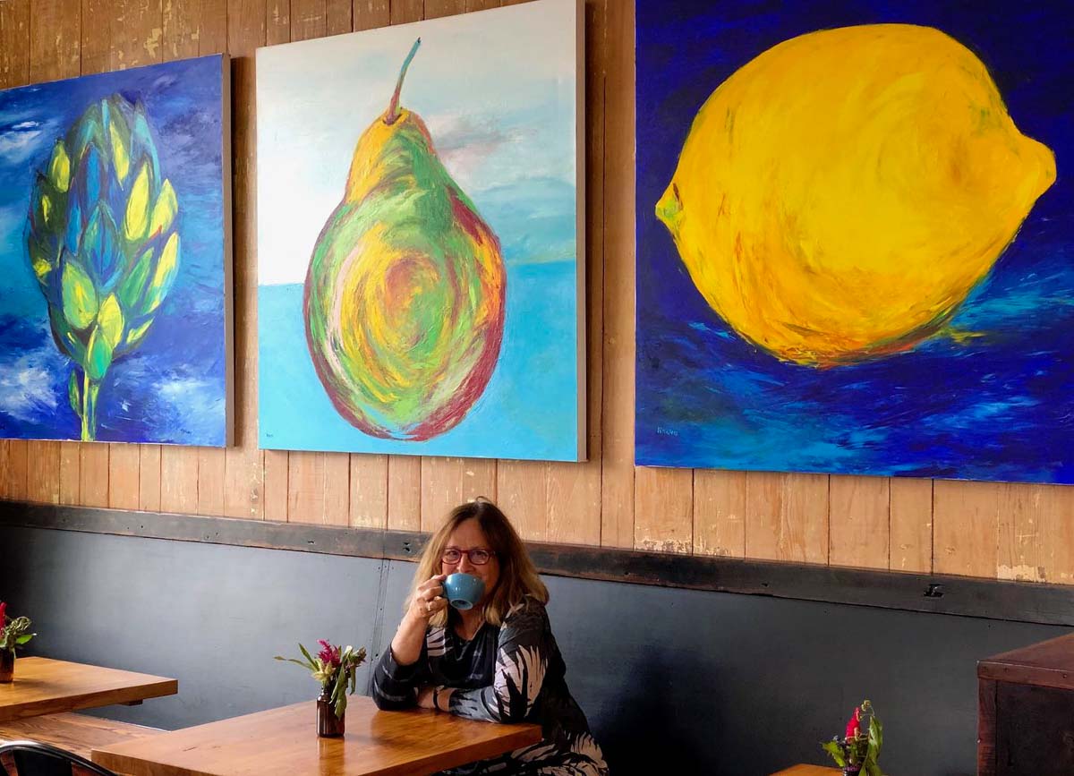  Artist Naava Koblenz at a cafe in front of 3 of her works.